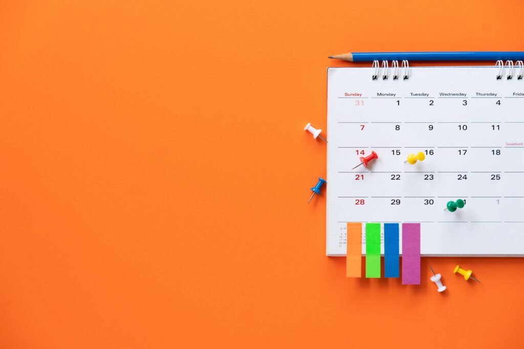 An orange background with a calendar with sticky markers and pins on how to manage changing holiday demand for distributors
