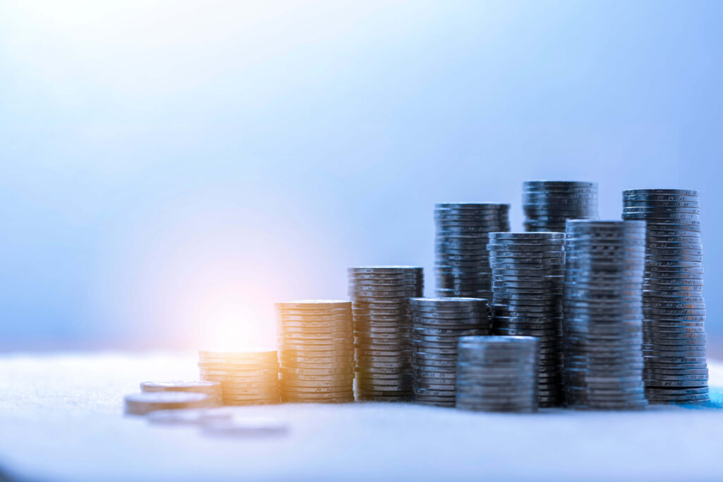 Piles of coins of different heights on a blue background with light shining on the two of the piles 5 inventory reduction methods to deliver cost savings