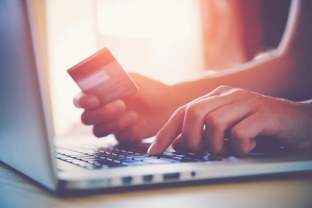 A close up of a person's hands using a laptop, typing with left hand and holding a credit card in the right hand. ecommerce inventory management. online inventory management.
