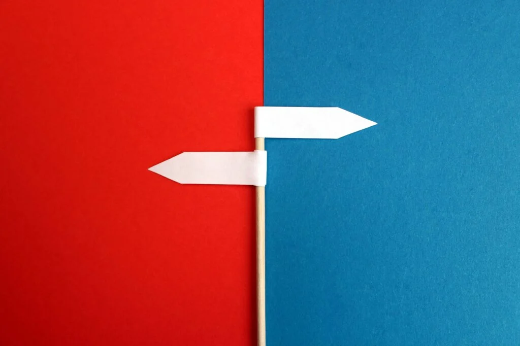 A white pole with a white arrow road sign pointing left, just under a white arrow road sign pointing right. The left-facing arrow is on a red background, and the right-facing arrow is on a blue background. What's better? You ERP system or inventory optimisation software?