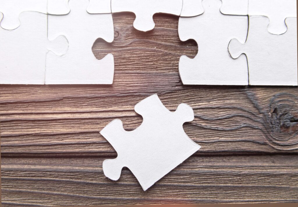 A white jigsaw on a wooden table with one piece not complete and just below at an angle to show erp connections erp apps