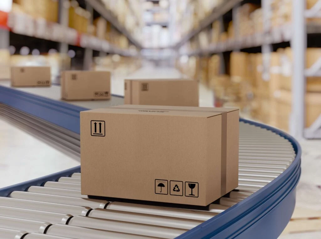 Cardboard boxes flowing down a production line roller conveyor belt with a blurred background of a warehouse to show stock turnover