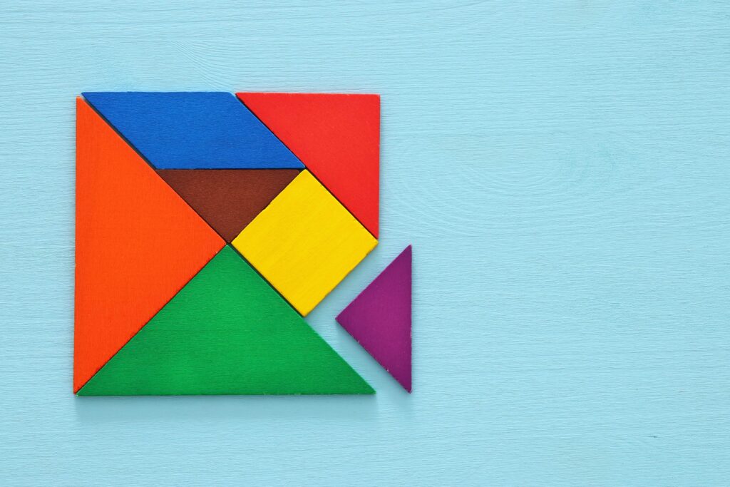 A puzzle made up of different coloured wooden pieces in different shapes put together to form a square on a blue background to show challenges in inventory planning