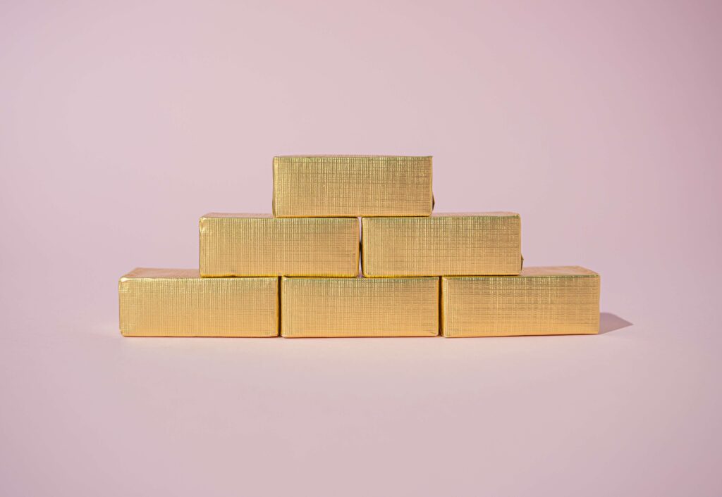 Gold bars stacked three on the bottom, two in the middle and one on the top on a pink background to show a bell curve of a product lifecycle
