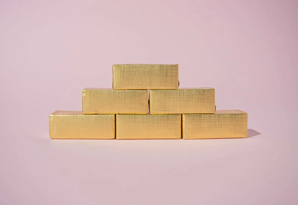 Gold bars stacked three on the bottom, two in the middle and one on the top on a pink background to show a bell curve of a product lifecycle
