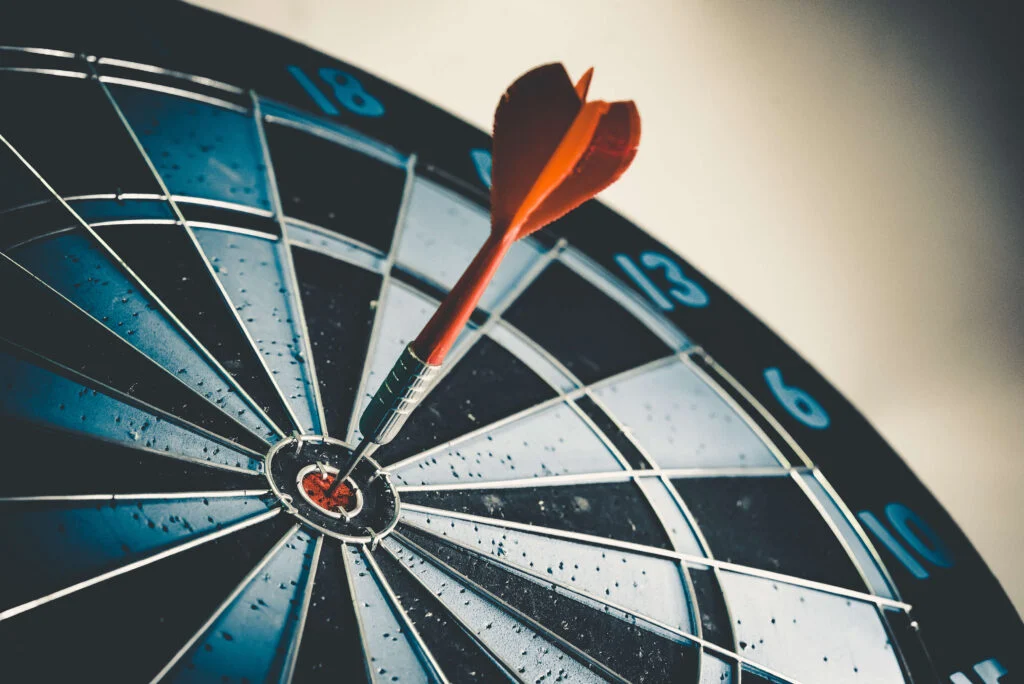 A close up of a dart board lying slightly to the left on a light background with one red dart in the bullseye to show inventory KPIs