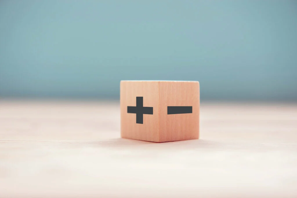 A wooden dice with a plus sign on one side and minus sign on the adjacent side on a wooden table next to a light blue wall what are the fundamental differences between jut-in-time and just-in-case stock control