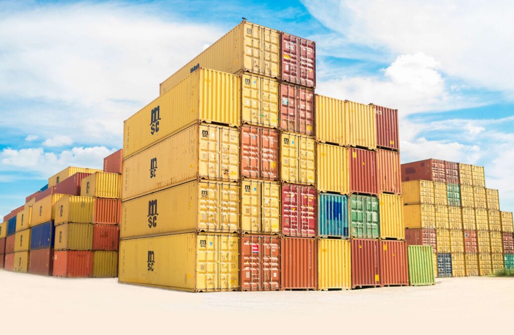 A variety of colourful shipping containers stacked in a shipping yard five high and at different heights with blue sky and white clouds