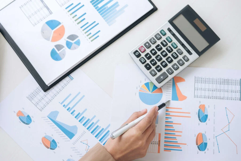 A table covered in charts with a person's hand, a calculator and a pen Het belang van optimale inkoopplanning