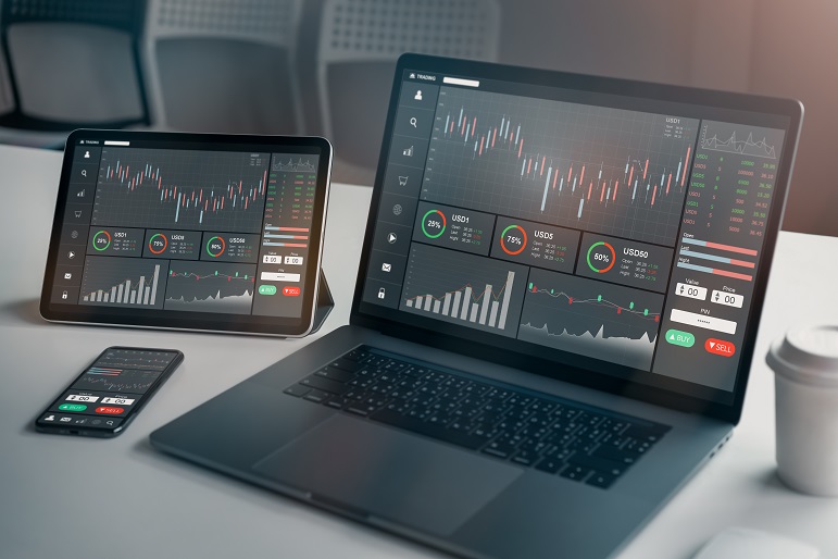 A black latop, tablet and mobile phone on a table with a coffee cup and mouse showing stock market tracking charts and data to show data analysis