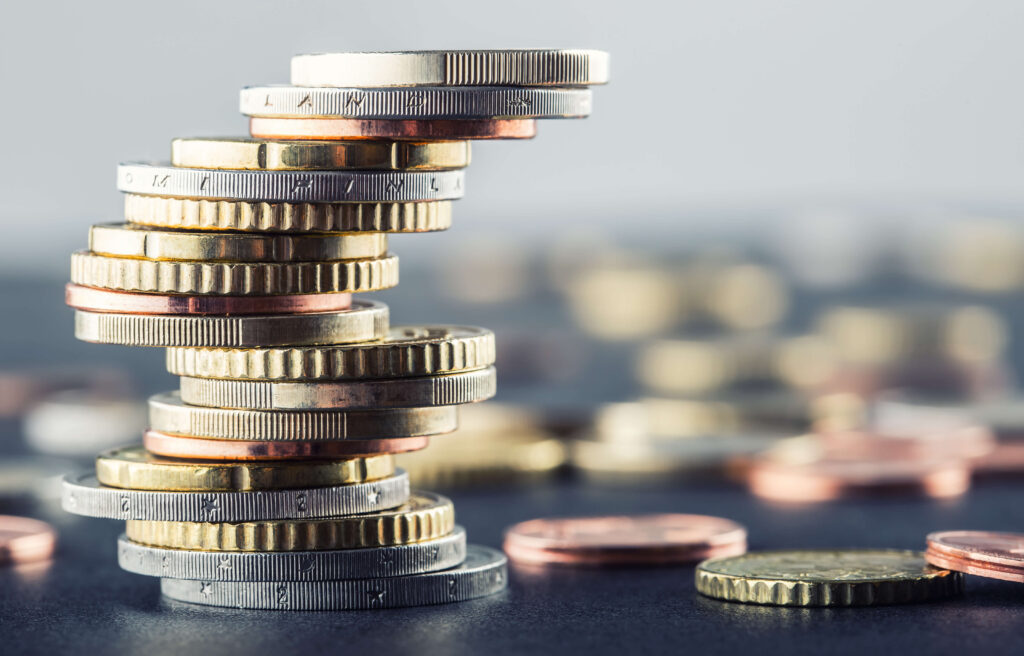 Different coloured coins balancing in a pile with others scattered on a table.