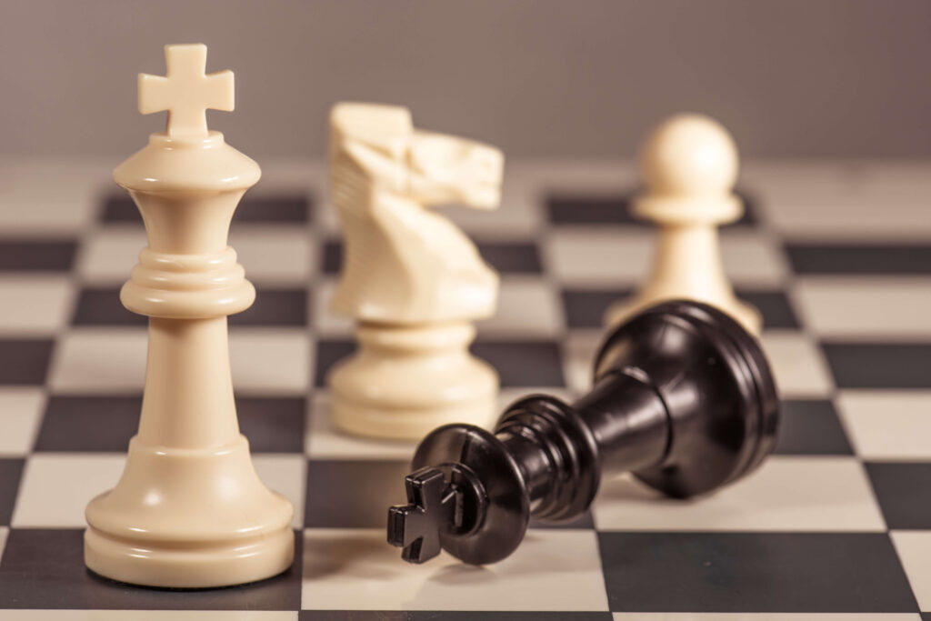 Close up of a chess board with a white queen, knight and pawn next to a black queen on its side supply chain strategies supply chain risk mitigation